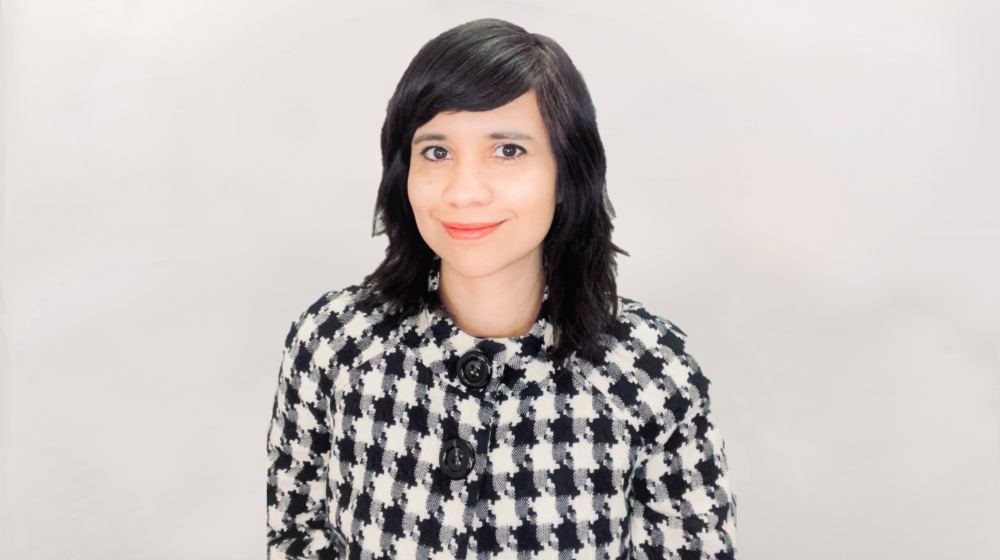 Professional headshot of a smiling woman with shoulder-length dark hair wearing a patterned jacket against a light background